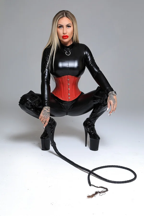 Crouching down in her black latex outfit Mistress Paola is also holding her whip 